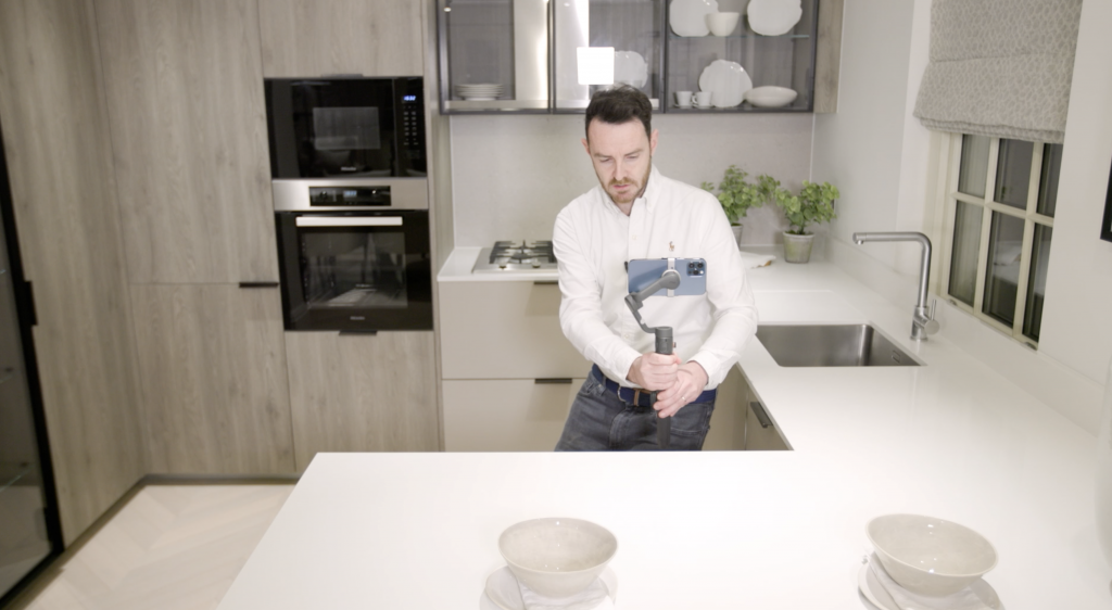 A image of a real estate agent filming a real estate video on a gimbal in a kitchen.