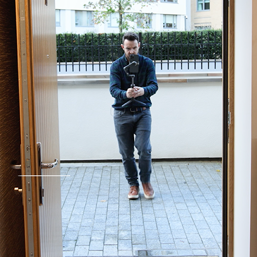 An image of a real estate filming on a gimbal entering a property through the front door.